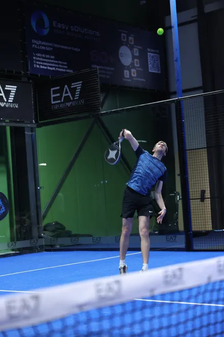 A player stretching for an overhead in front of the EA7 Emporio Armani boards