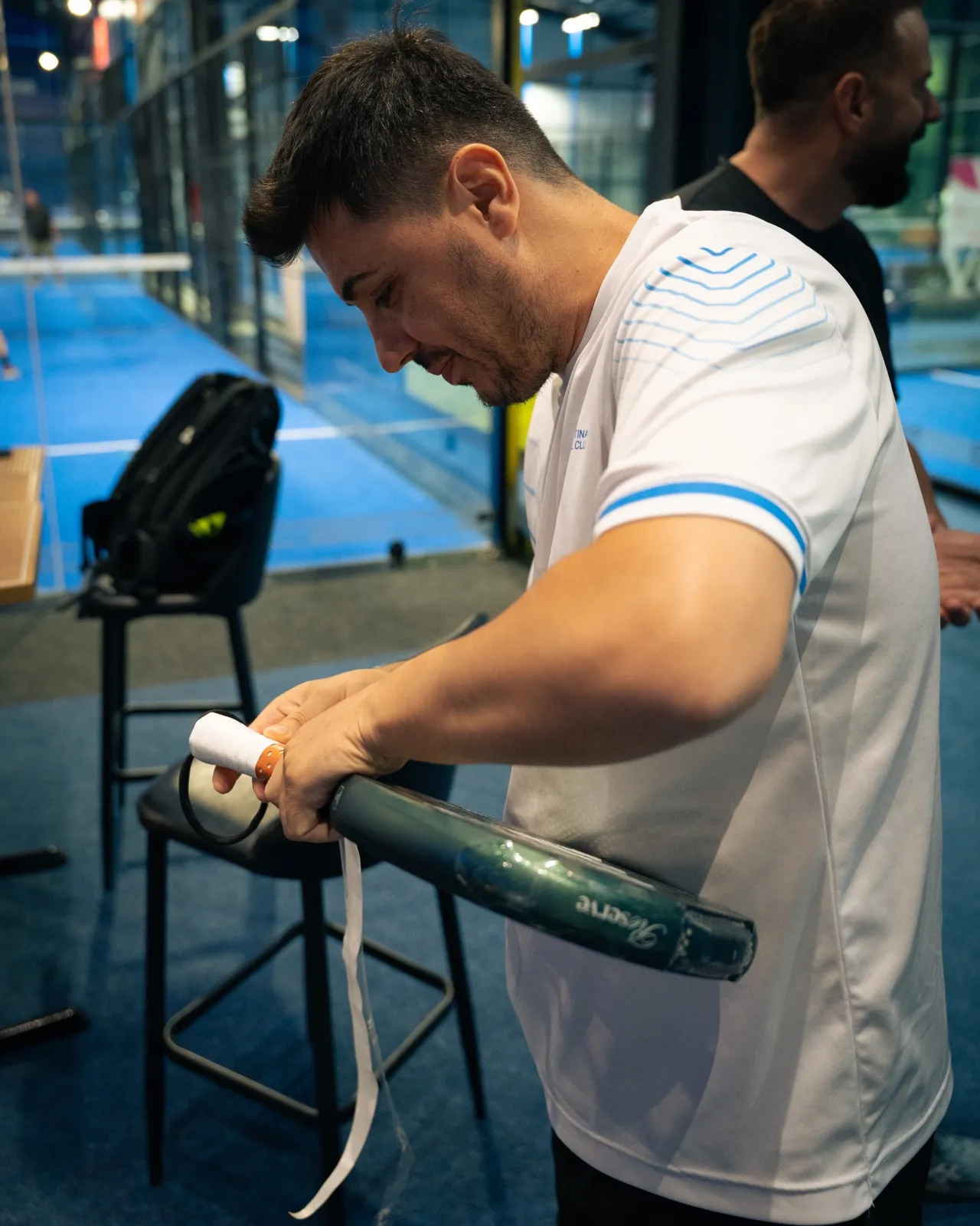 Player wrapping a fresh overgrip onto a padel racket courtside at Padel Zone Prishtina