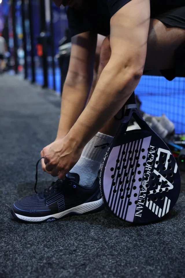A player lacing EA7 shoes beside an EA7 racket before a match