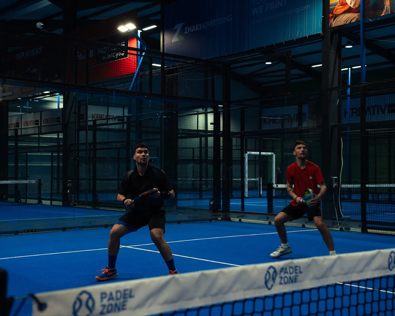 Two padel players in ready position at the net on an indoor court at Padel Zone Prishtina